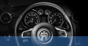 Black and white photo of car steering wheel with Module Master logo over it and dashboard instrument panel.